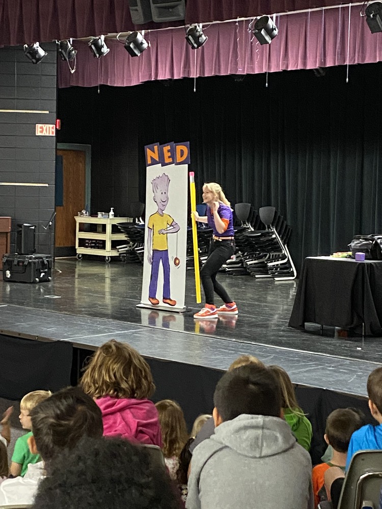 A Performer Stands on Stage as Students Watch the School Assembly Known as the NED Show