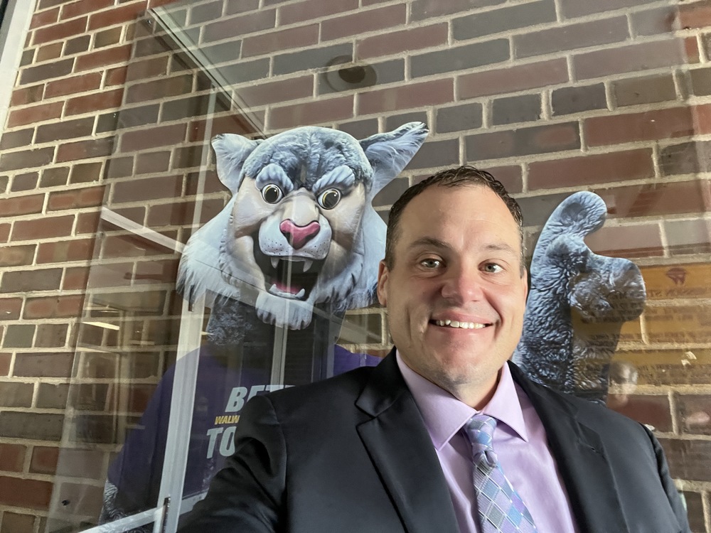 District Administrator Phill Klamm with a Photo of Wesley the Wildcat (School Mascot) in the Background