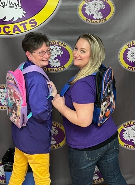 Mrs Coleman and Mrs Ott-Wilson Wearing Backpacks with the Walworth Wildcat Background