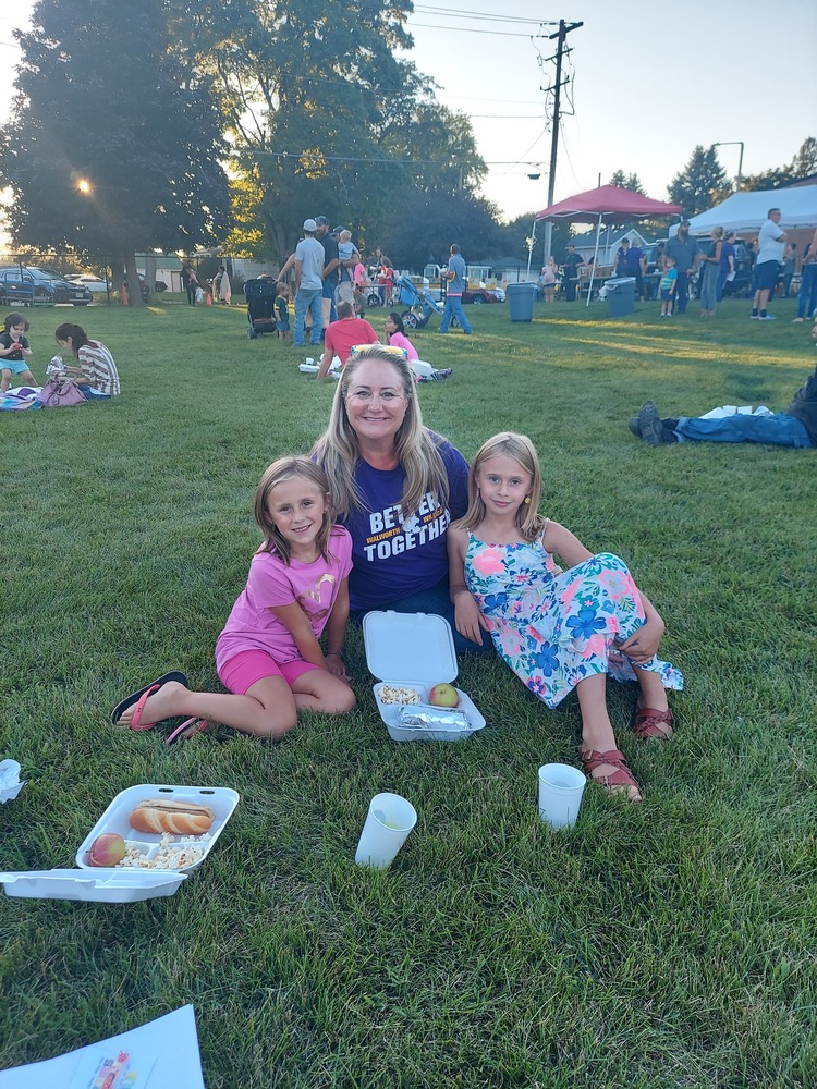 A family sits in the grass, picnic style, surrounded by other people